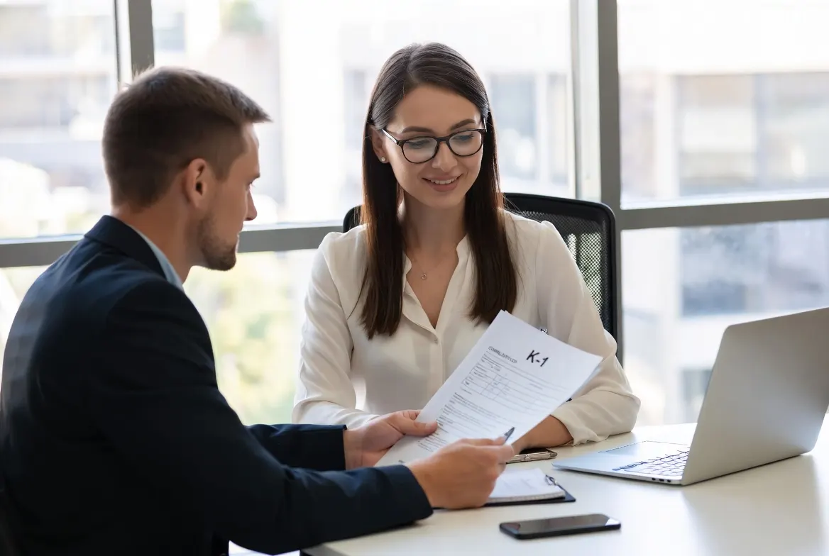 Two business partners seated at a conference table with a completed Schedule K-1 folder open between them and composed attentive expressions