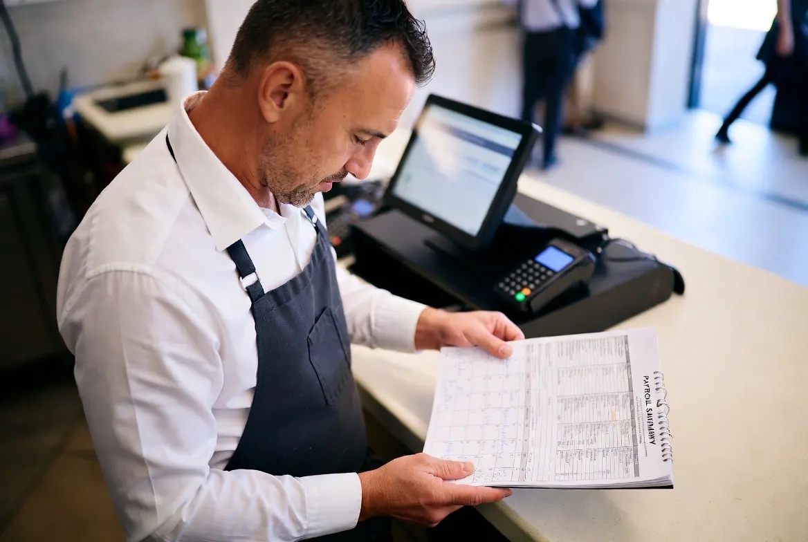 Restaurant owner reviewing a payroll calendar and payroll tax summary at the counter